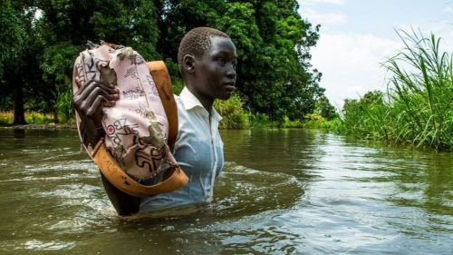Una niña sostiene sus libros para que no se mojen de camino a casa desde la escuela en la aldea de Walangwalang, que se salvó de las inundaciones del río, en las afueras de Juba, en Sudán del Sur